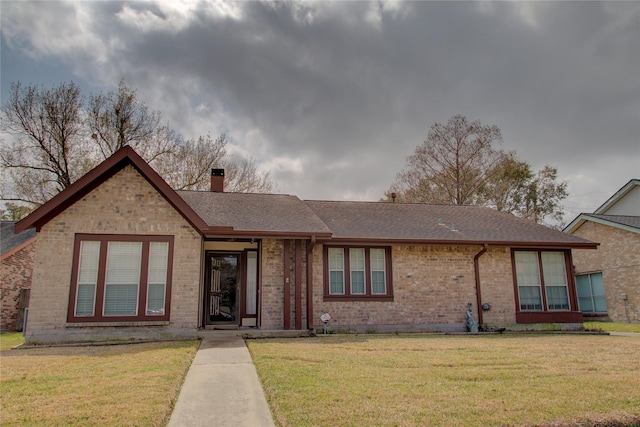 view of front of home with a front yard, roof with shingles, a chimney, and brick siding