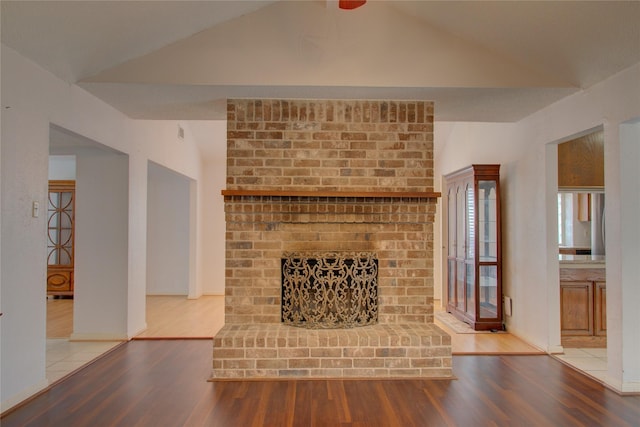 unfurnished living room with lofted ceiling, a brick fireplace, baseboards, and wood finished floors