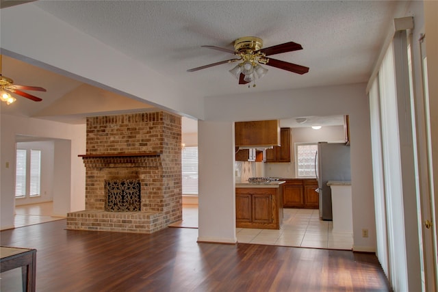 unfurnished living room featuring a ceiling fan, a fireplace, a textured ceiling, and light wood finished floors