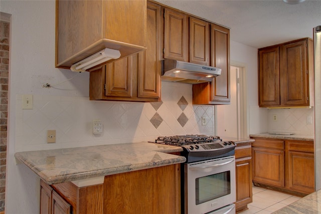 kitchen with light tile patterned floors, brown cabinetry, stainless steel range with gas cooktop, and under cabinet range hood