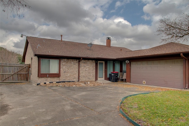 ranch-style house featuring driveway, a chimney, roof with shingles, an attached garage, and brick siding