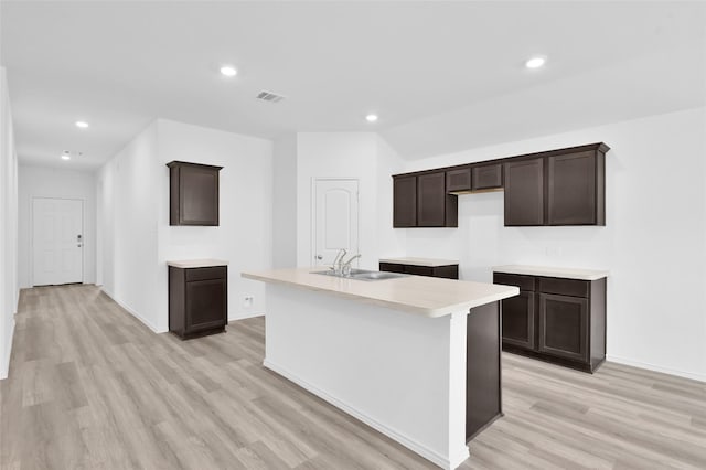 kitchen with visible vents, a kitchen island with sink, a sink, dark brown cabinets, and light wood-type flooring