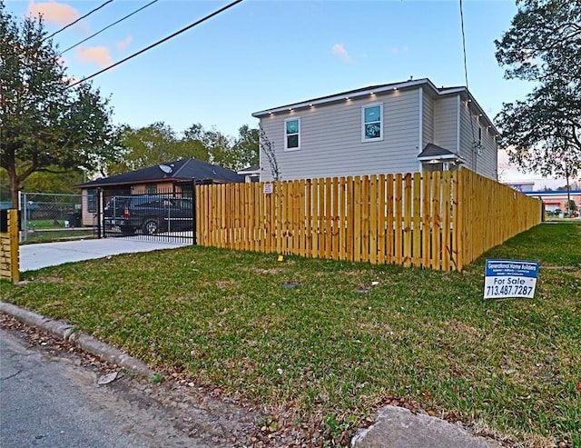 view of side of property with a yard, concrete driveway, and fence