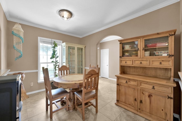 dining room featuring crown molding, light tile patterned floors, baseboards, and arched walkways