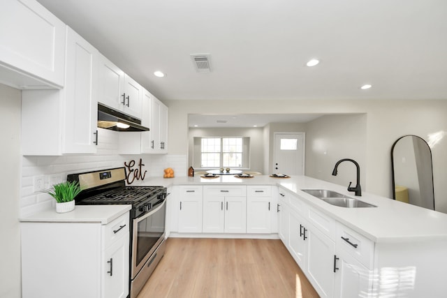 kitchen with a peninsula, stainless steel gas range, a sink, and under cabinet range hood