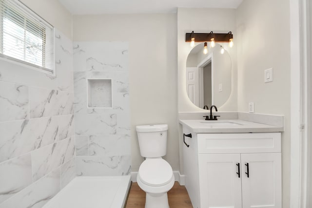 full bath with toilet, wood finished floors, vanity, baseboards, and a tile shower