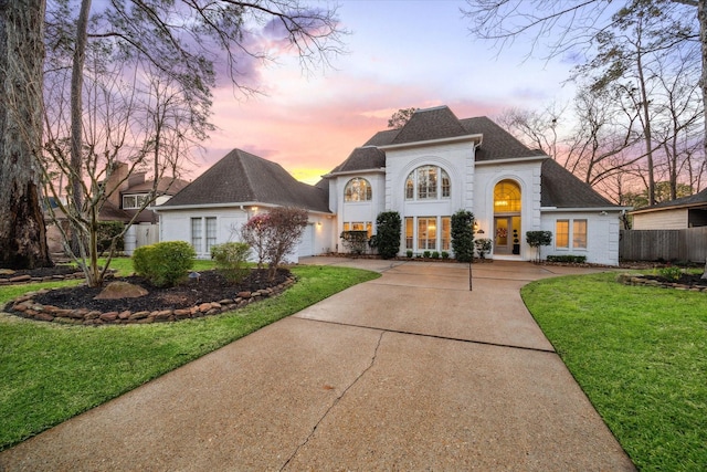 french country inspired facade with french doors, a front yard, fence, a garage, and driveway