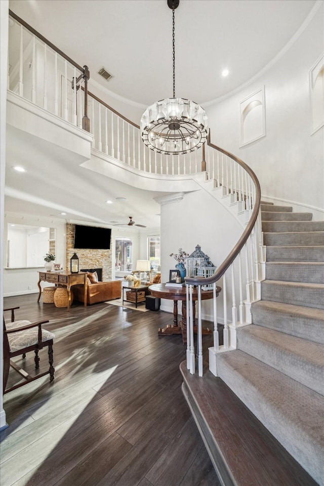 foyer entrance with visible vents, wood finished floors, a high ceiling, stairs, and a stone fireplace