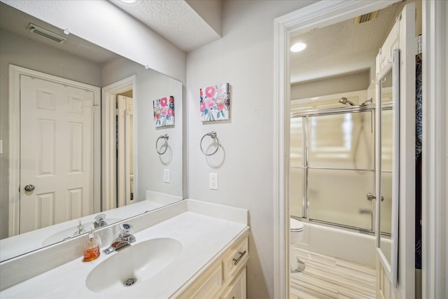 bathroom with visible vents, toilet, combined bath / shower with glass door, vanity, and a textured ceiling