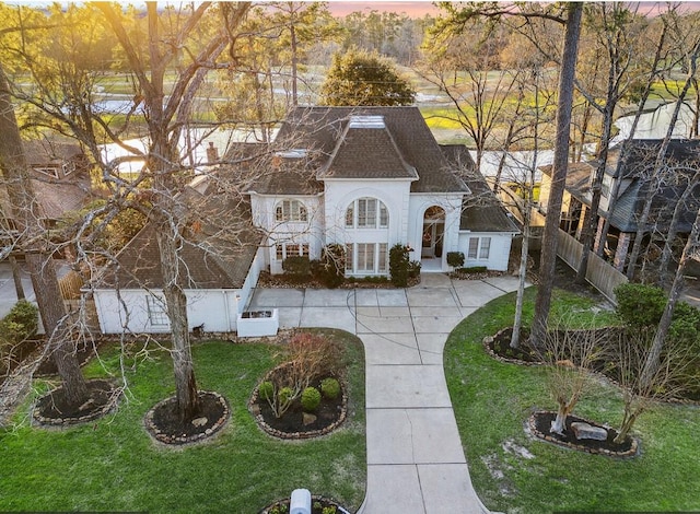 french provincial home featuring a front lawn, a shingled roof, fence, and stucco siding