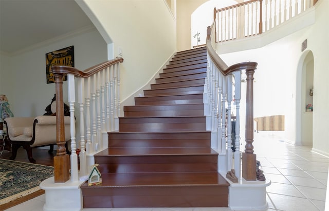 stairs with tile patterned flooring, a high ceiling, arched walkways, and ornamental molding