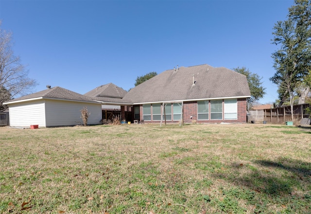 rear view of property with brick siding, fence, and a yard