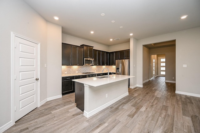 kitchen featuring stainless steel appliances, a sink, light wood-style floors, light countertops, and tasteful backsplash