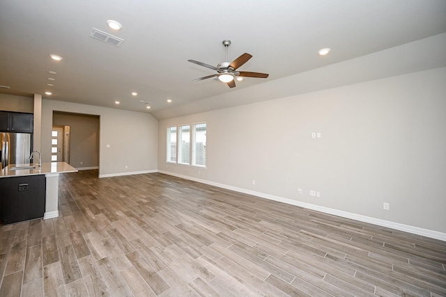 unfurnished living room with light wood finished floors, baseboards, visible vents, a sink, and recessed lighting