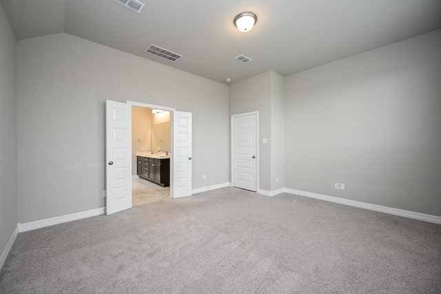 unfurnished bedroom featuring visible vents, ensuite bathroom, light carpet, vaulted ceiling, and baseboards