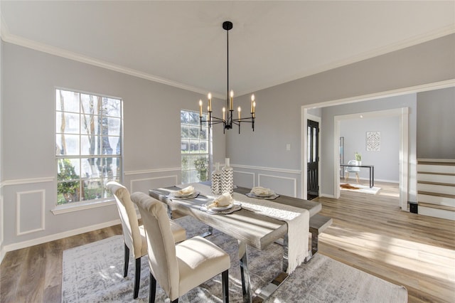 dining area with a chandelier, a decorative wall, a wainscoted wall, wood finished floors, and crown molding