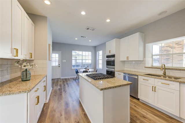 kitchen with visible vents, a kitchen island, appliances with stainless steel finishes, white cabinetry, and a sink