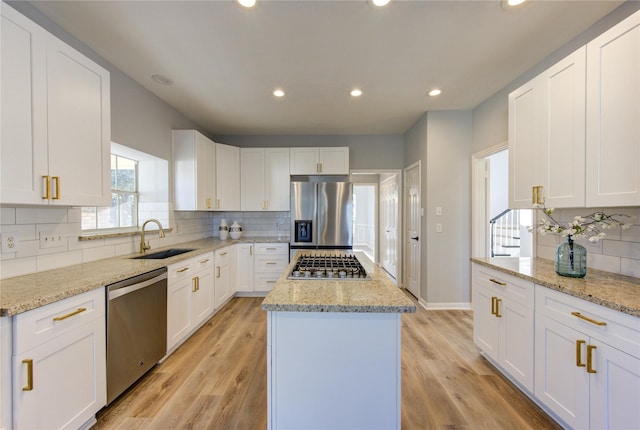 kitchen with stainless steel appliances, a kitchen island, a sink, light wood-style floors, and tasteful backsplash