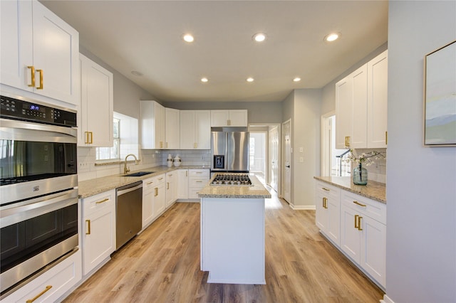 kitchen featuring decorative backsplash, appliances with stainless steel finishes, a sink, a kitchen island, and light wood-type flooring