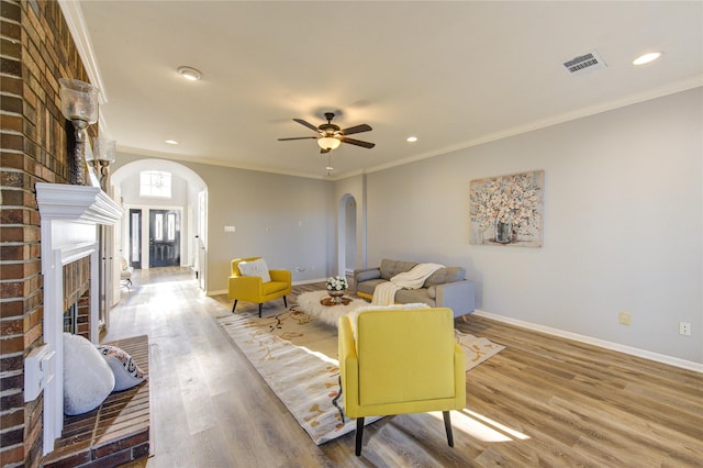 living room featuring arched walkways, wood finished floors, visible vents, baseboards, and ornamental molding