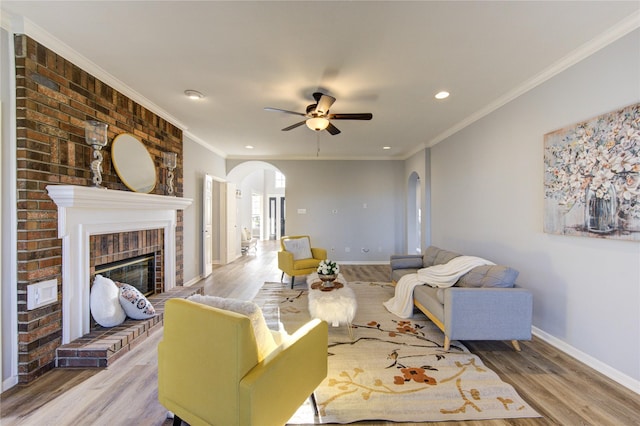 living area with arched walkways, crown molding, a brick fireplace, wood finished floors, and baseboards