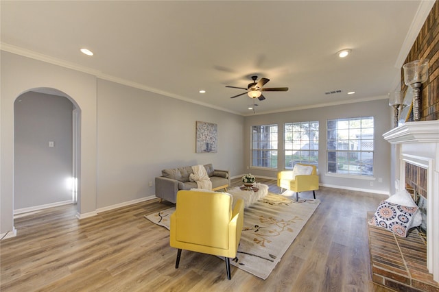 living room with a brick fireplace, arched walkways, wood finished floors, and ornamental molding