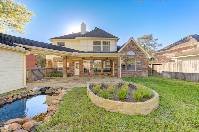 rear view of house featuring a lawn, a fenced backyard, a chimney, a patio area, and brick siding