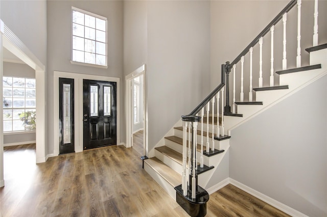 foyer with stairs, a towering ceiling, baseboards, and wood finished floors