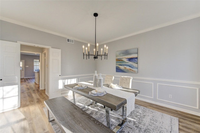 dining space with light wood-type flooring, visible vents, a notable chandelier, and ornamental molding