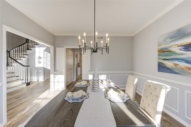 dining room featuring a decorative wall, crown molding, wood finished floors, stairs, and an inviting chandelier