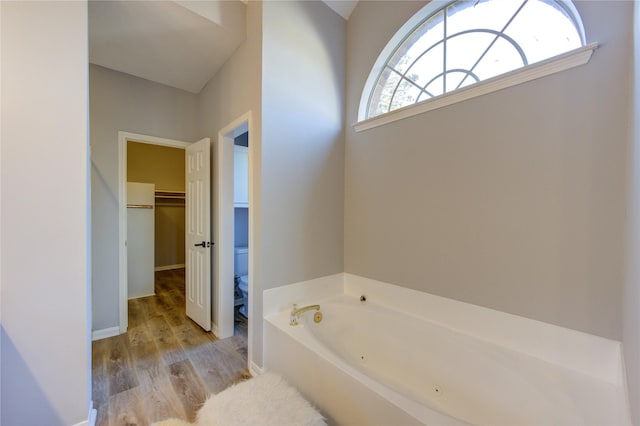 bathroom with a garden tub, toilet, wood finished floors, baseboards, and a walk in closet