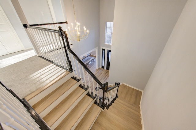 stairs featuring baseboards, wood finished floors, a towering ceiling, and an inviting chandelier