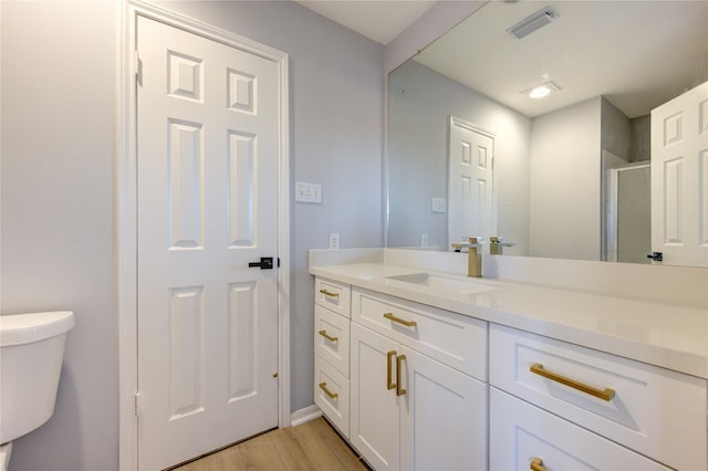 bathroom with toilet, wood finished floors, vanity, visible vents, and a shower stall