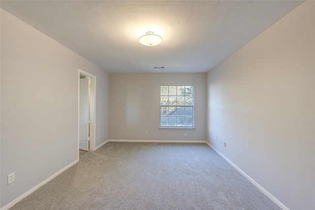 spare room featuring carpet floors, visible vents, a textured ceiling, and baseboards