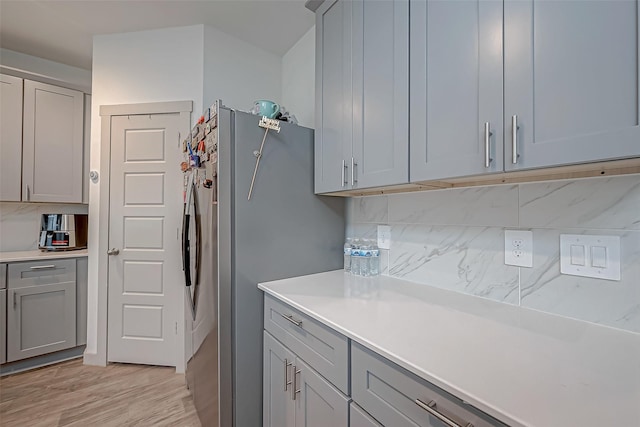 kitchen featuring light countertops, stainless steel fridge, backsplash, and gray cabinetry