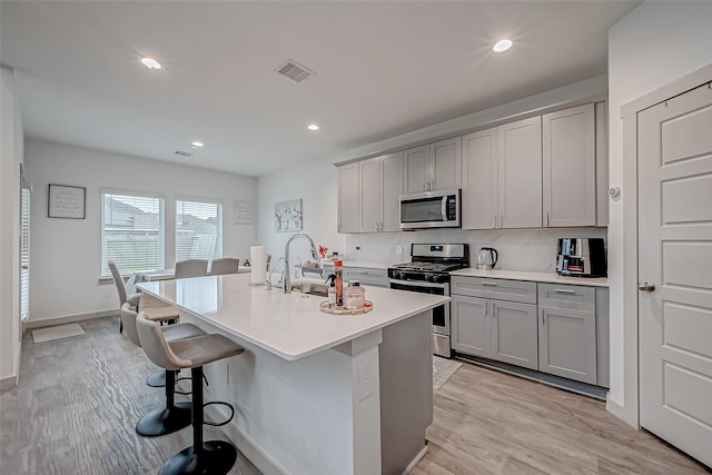 kitchen with a breakfast bar, a sink, visible vents, appliances with stainless steel finishes, and gray cabinets