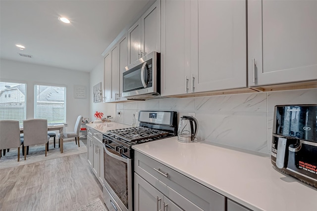 kitchen featuring gray cabinets, light countertops, decorative backsplash, appliances with stainless steel finishes, and light wood-style floors