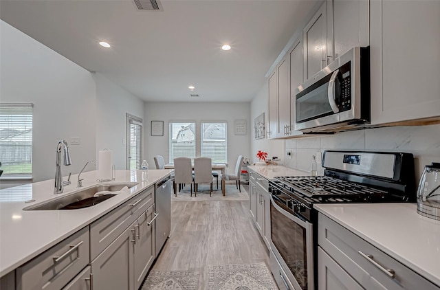 kitchen featuring stainless steel appliances, tasteful backsplash, gray cabinets, light countertops, and a sink