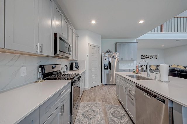 kitchen featuring appliances with stainless steel finishes, light countertops, a sink, and gray cabinetry