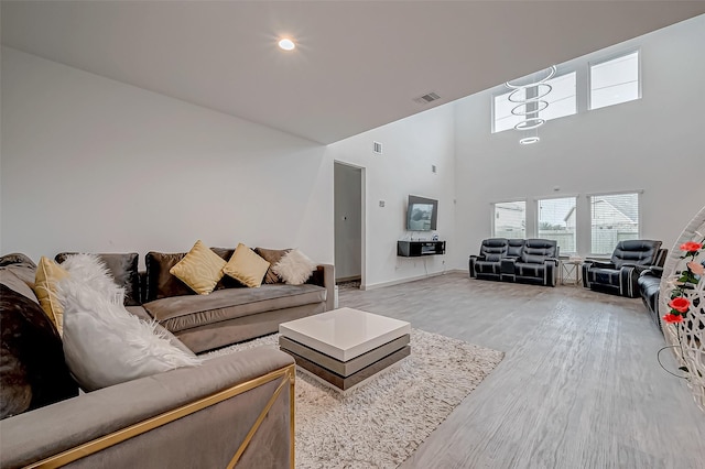 living area with a towering ceiling, light wood finished floors, and visible vents