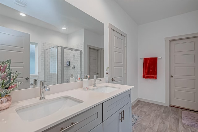 bathroom with double vanity, wood finished floors, a sink, and a shower stall