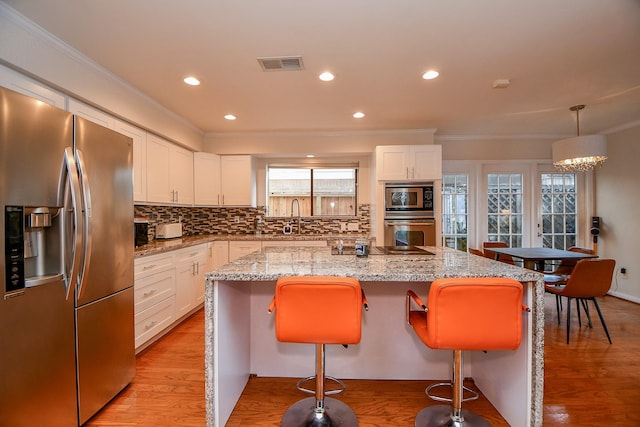 kitchen featuring visible vents, a sink, stainless steel appliances, light wood-type flooring, and a center island