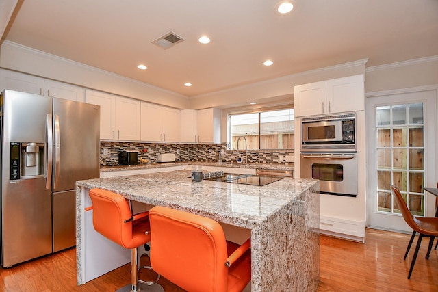 kitchen featuring visible vents, ornamental molding, backsplash, a kitchen island, and appliances with stainless steel finishes