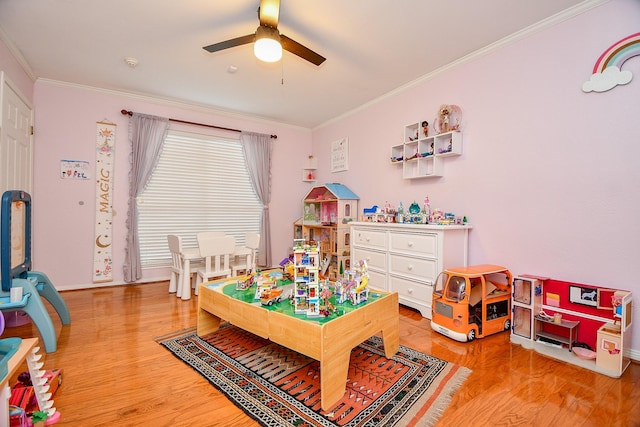 playroom with crown molding, a ceiling fan, light wood-type flooring, and baseboards