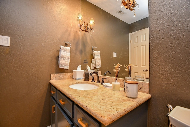 bathroom featuring visible vents, vanity, an inviting chandelier, and a textured wall