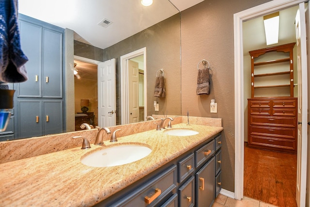 full bath featuring double vanity, a textured wall, visible vents, and a sink