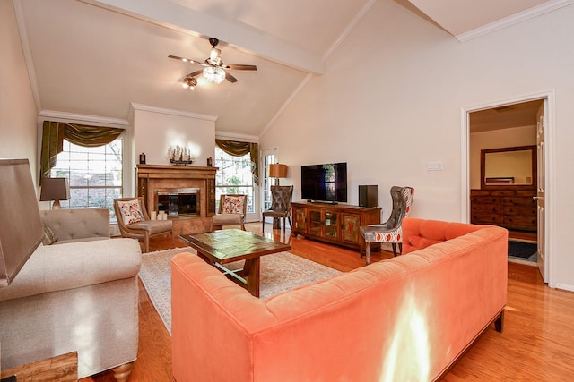 living room featuring light wood finished floors, crown molding, beam ceiling, a fireplace, and a ceiling fan