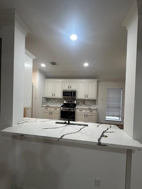 kitchen with a peninsula, a sink, visible vents, appliances with stainless steel finishes, and decorative backsplash