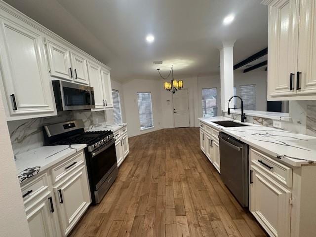 kitchen featuring appliances with stainless steel finishes, wood finished floors, a sink, white cabinetry, and a notable chandelier