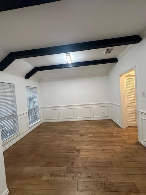 unfurnished room featuring beam ceiling, visible vents, wainscoting, and wood finished floors